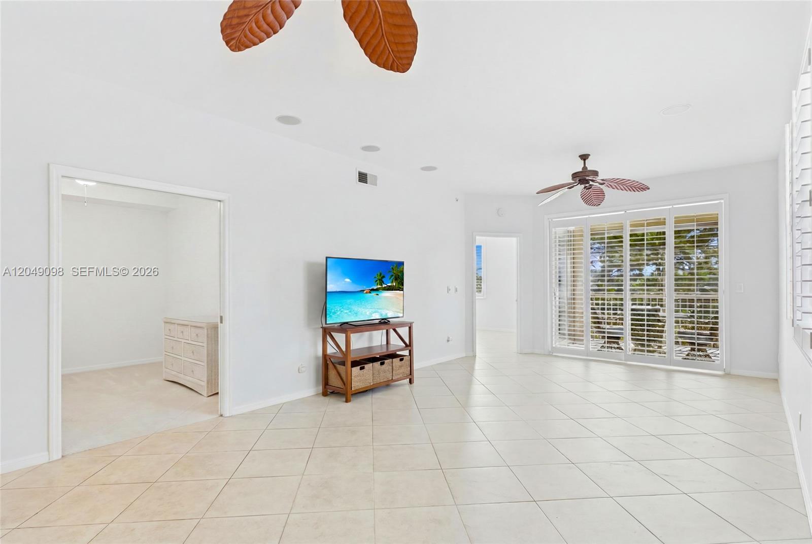 A bright living room features white walls, tile flooring, a ceiling fan, and sliding doors — BONITA SPRINGS, FL