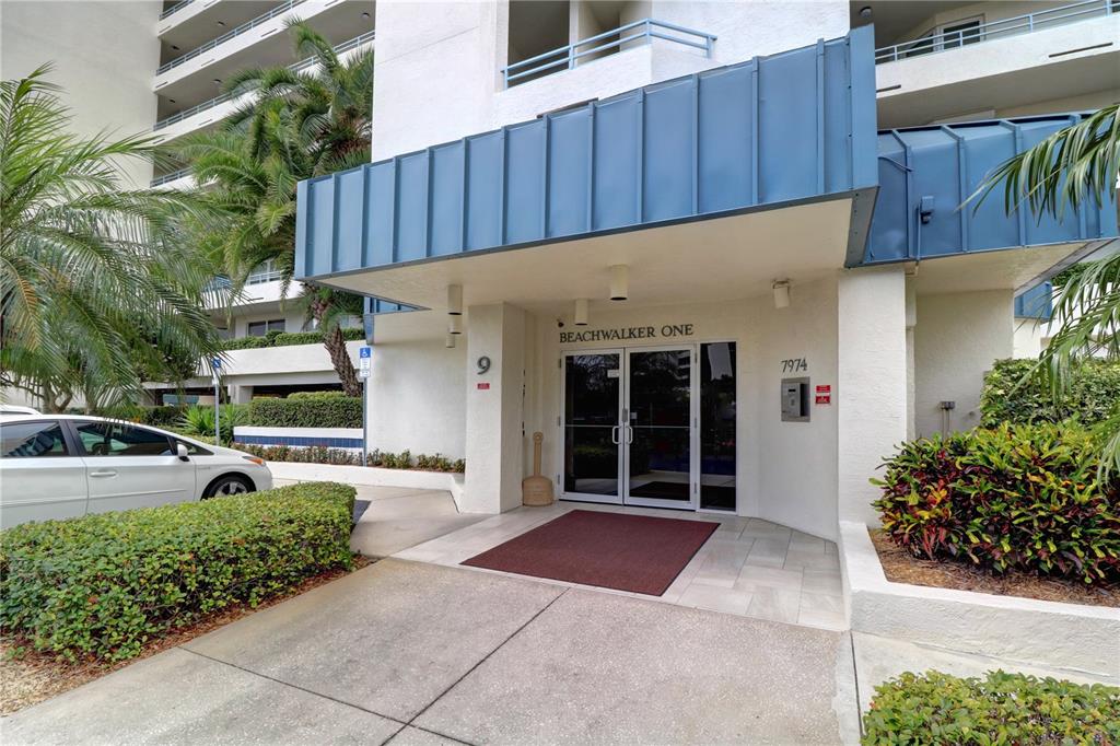 The exterior entrance of a multi-story residential building features a blue metal awning — 7974 SAILBOAT KEY BOULEVARD S UNIT 701, SOUTH PASADENA, FL