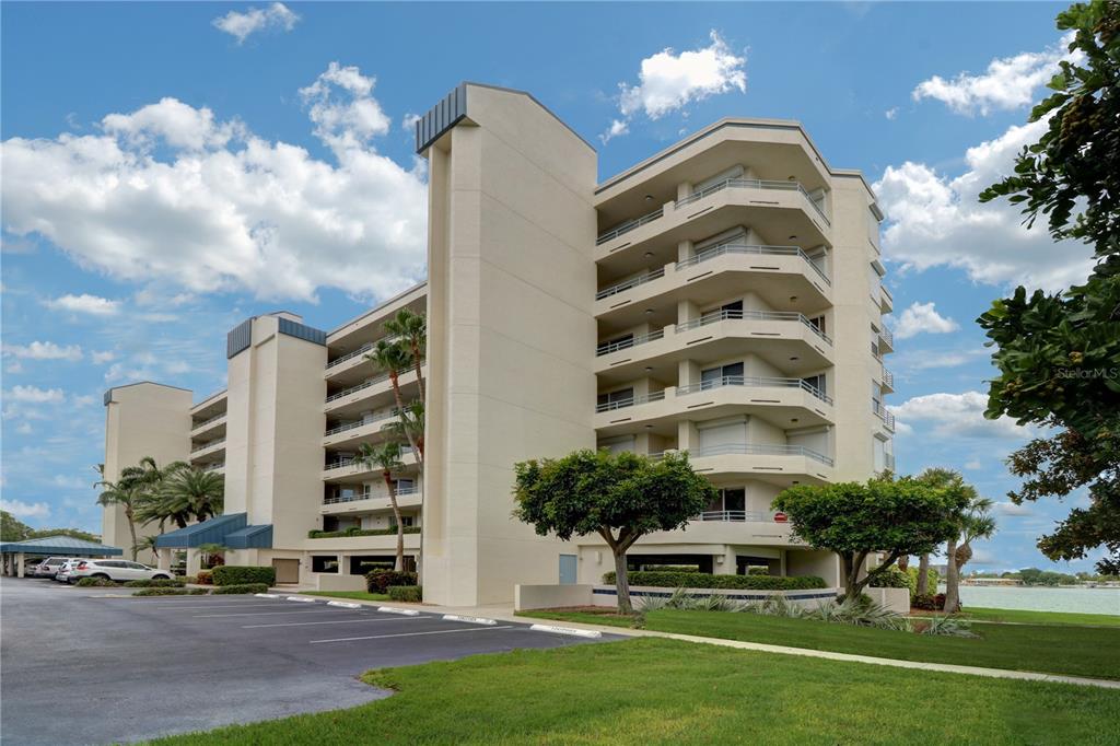 A multi-story beige apartment building with balconies stands next to a parking lot and lawn — 7974 SAILBOAT KEY BOULEVARD S UNIT 701, SOUTH PASADENA, FL
