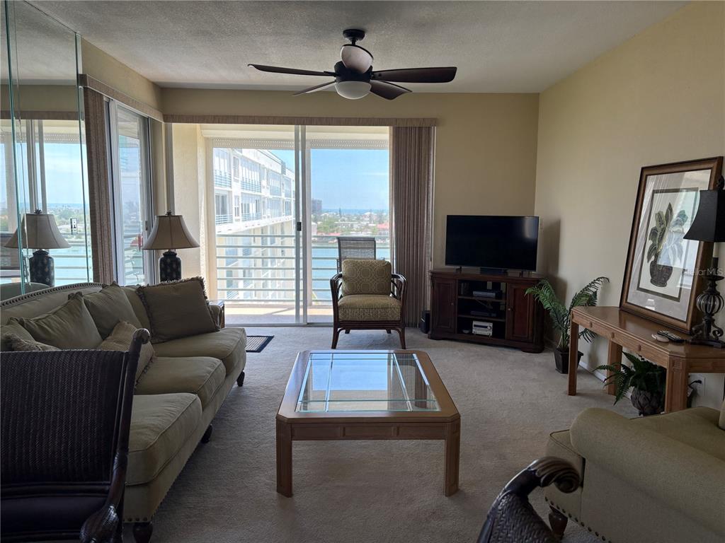 A living room features a glass-topped coffee table, beige sofa, and a balcony with water views — 7974 SAILBOAT KEY BOULEVARD S UNIT 701, SOUTH PASADENA, FL