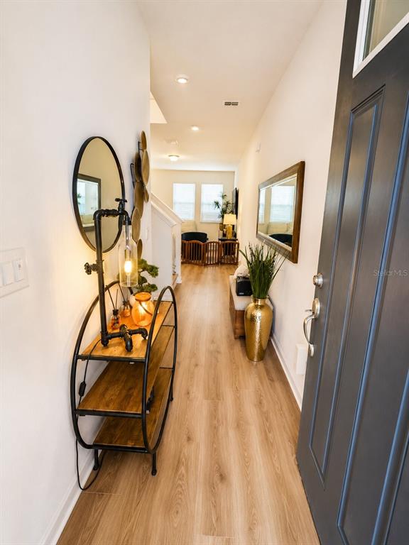 A hallway features wood-look flooring, a round mirror, a metal shelving unit, and a gold vase — 15613 WILLOW ARBOR CIRCLE, ORLANDO, FL