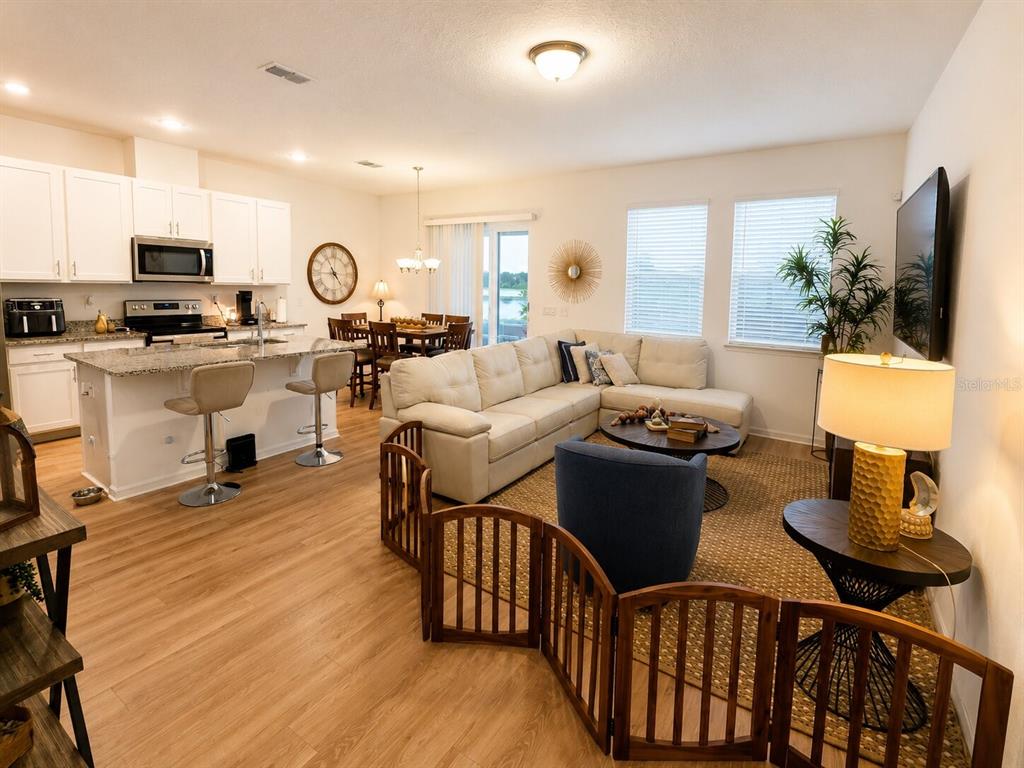 An open-concept living room and kitchen featuring white cabinetry, granite countertops, and light wood flooring — 15613 WILLOW ARBOR CIRCLE, ORLANDO, FL