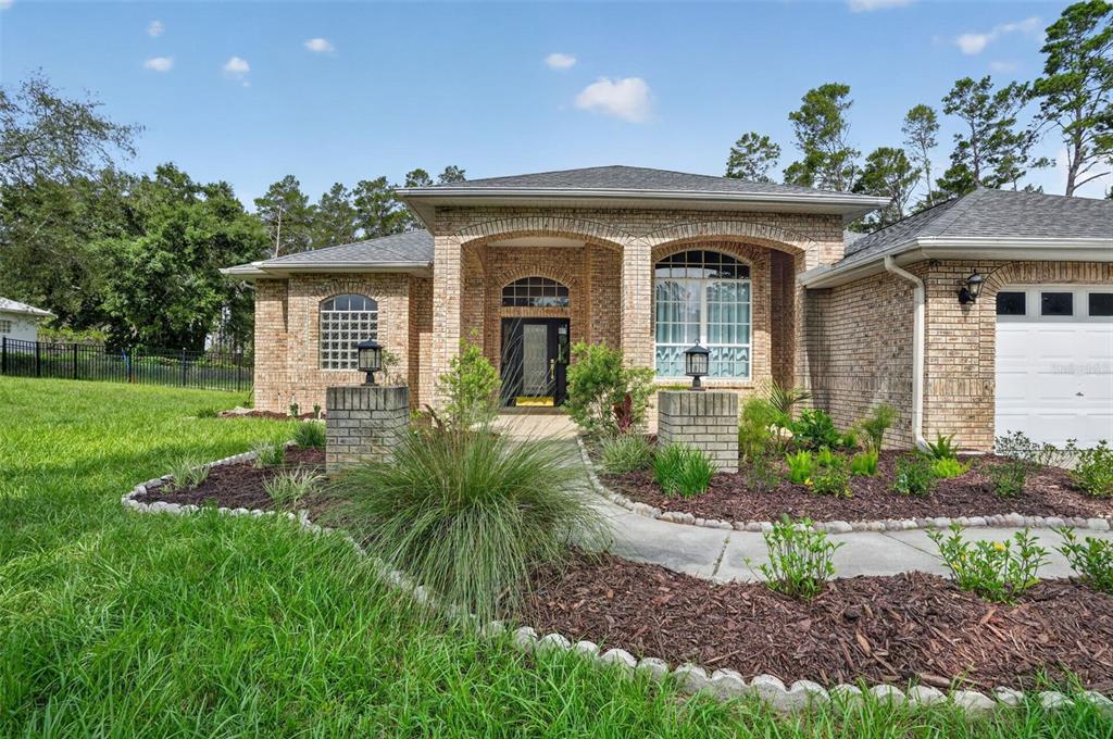 A brick single-story house features an arched entryway, a concrete walkway, and a landscaped yard — 9363 TOOKE SHORE DRIVE, WEEKI WACHEE, FL