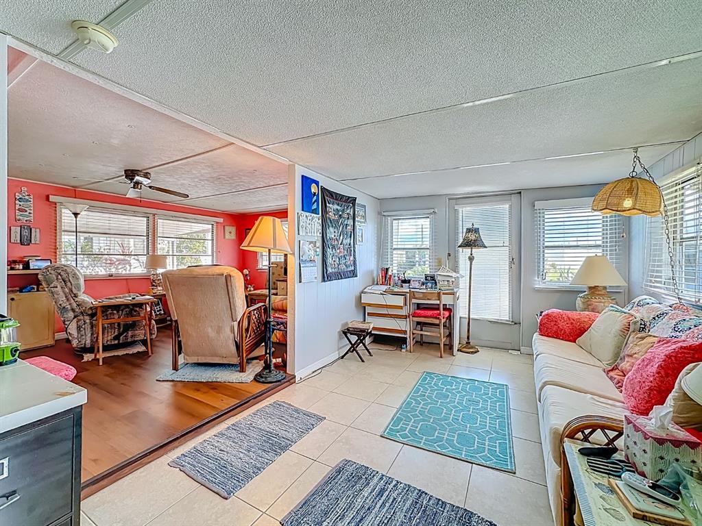A living room with a tiled floor, a sofa, and an adjacent room with wood flooring — 411 TROPIC DRIVE W, PALMETTO, FL