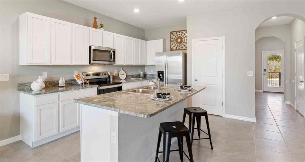 A kitchen features white cabinets, granite countertops, a center island with stools, and stainless appliances — 32202 TURTLE GRACE LOOP, WESLEY CHAPEL, FL