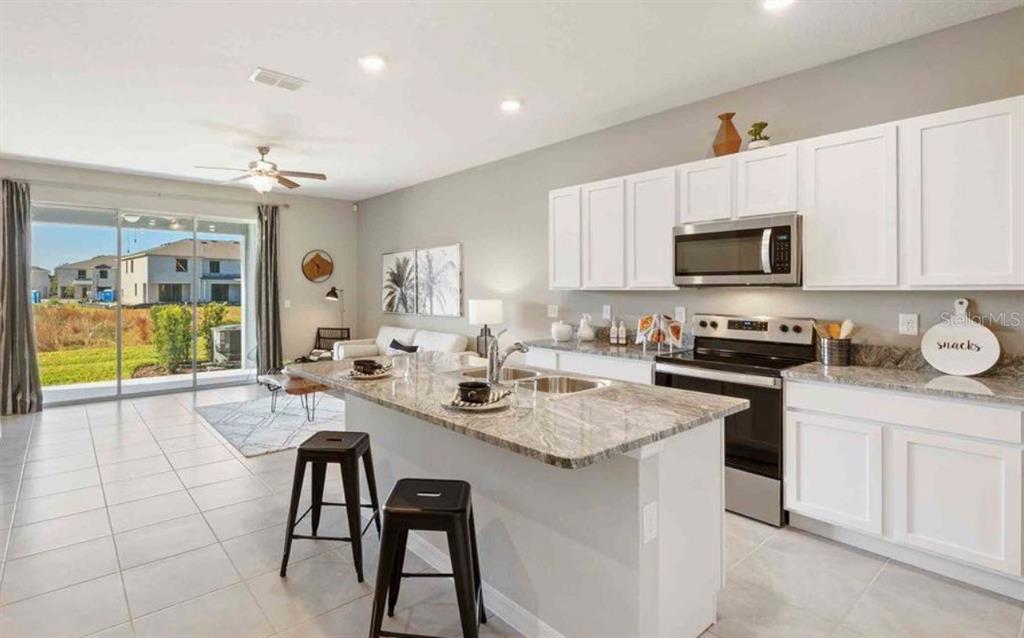 A kitchen with white cabinets and granite countertops overlooks a living area with sliding doors — 32202 TURTLE GRACE LOOP, WESLEY CHAPEL, FL