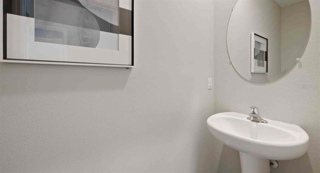 A powder room features a pedestal sink, a round mirror, and framed wall art — 32202 TURTLE GRACE LOOP, WESLEY CHAPEL, FL
