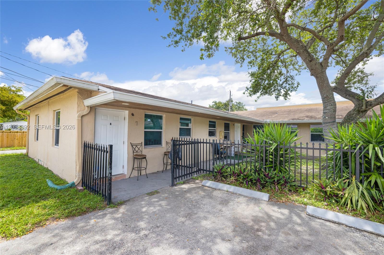 A single-story tan building features a white door, black metal fencing, and a paved driveway — 2247 Simms St, Hollywood FL 33020, HOLLYWOOD, FL