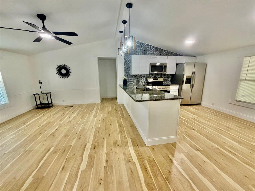 A kitchen with white cabinets, granite countertops, and patterned backsplash opens to a living area — 31638 LAKE DRIVE, EUSTIS, FL
