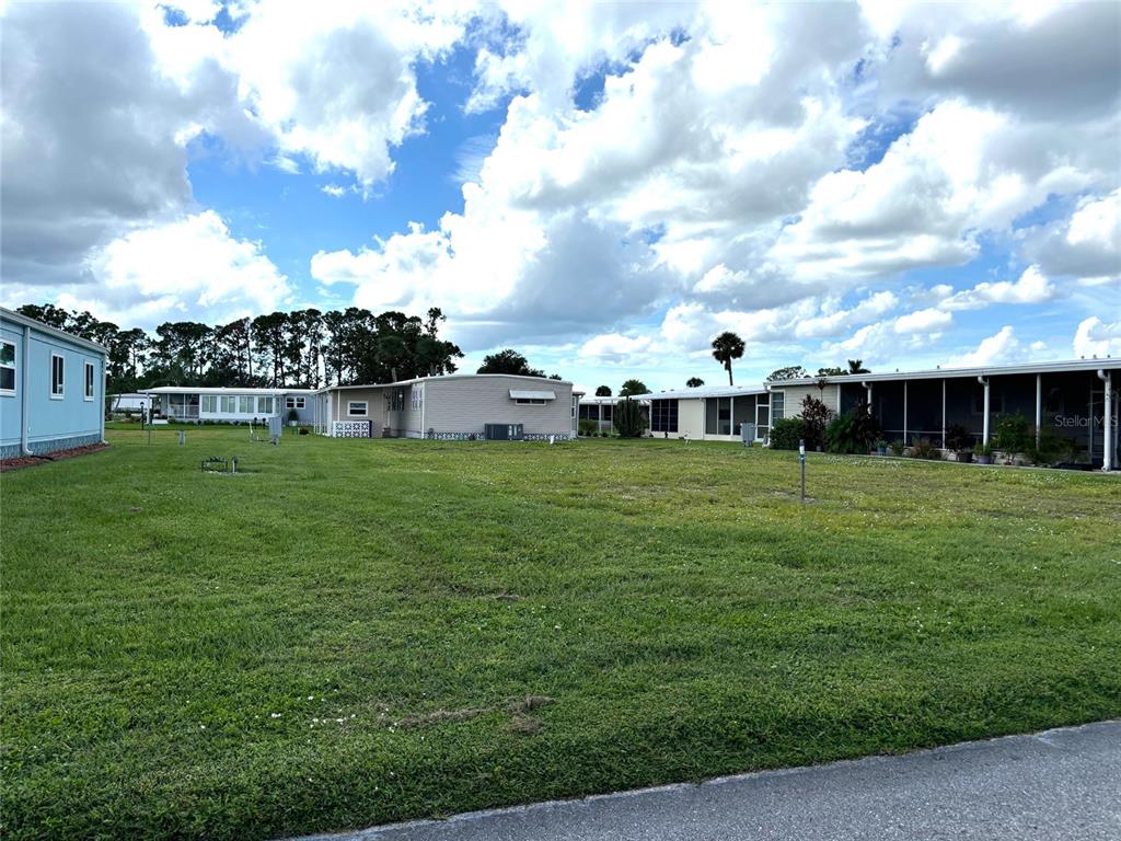 A grassy lot sits between several manufactured homes under a cloudy blue sky — 420 MADONNA, NORTH PORT, FL