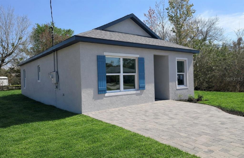 A single-story house with light gray stucco siding, blue shutters, and a paved driveway — 939 MOTON AVENUE, SANFORD, FL