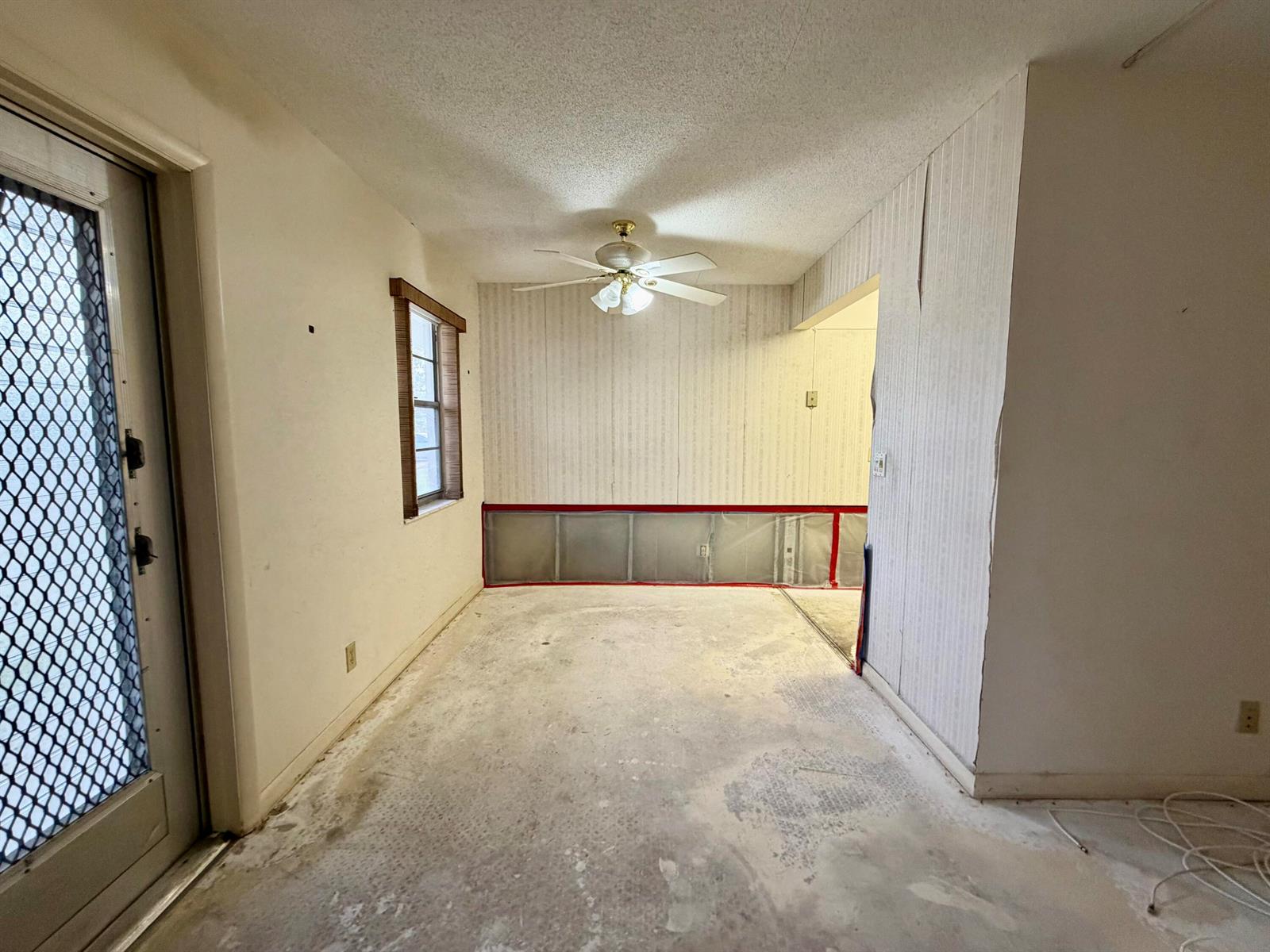 An unfinished room features a ceiling fan, wallpapered walls, a window, and exposed concrete flooring — 55 Hastings D, West Palm Beach FL 33417, WEST PALM BEACH, FL