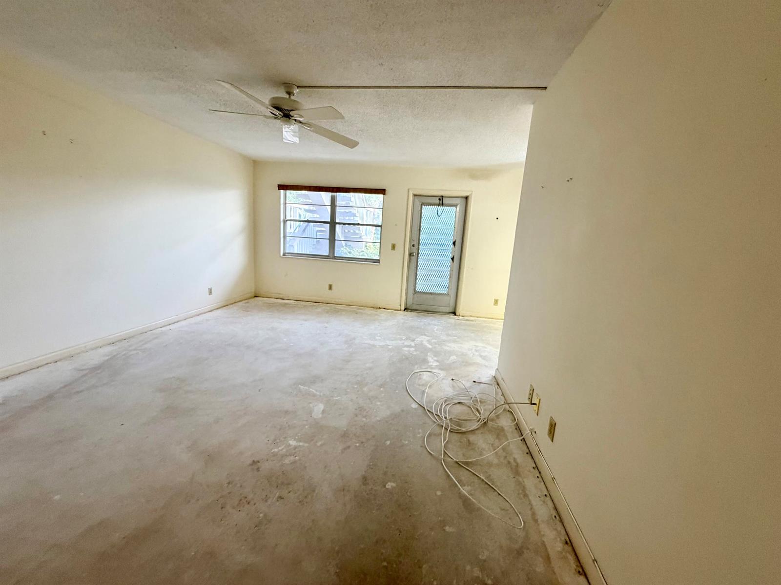 An empty room with a ceiling fan, a window, a door, and bare concrete flooring — 55 Hastings D, West Palm Beach FL 33417, WEST PALM BEACH, FL