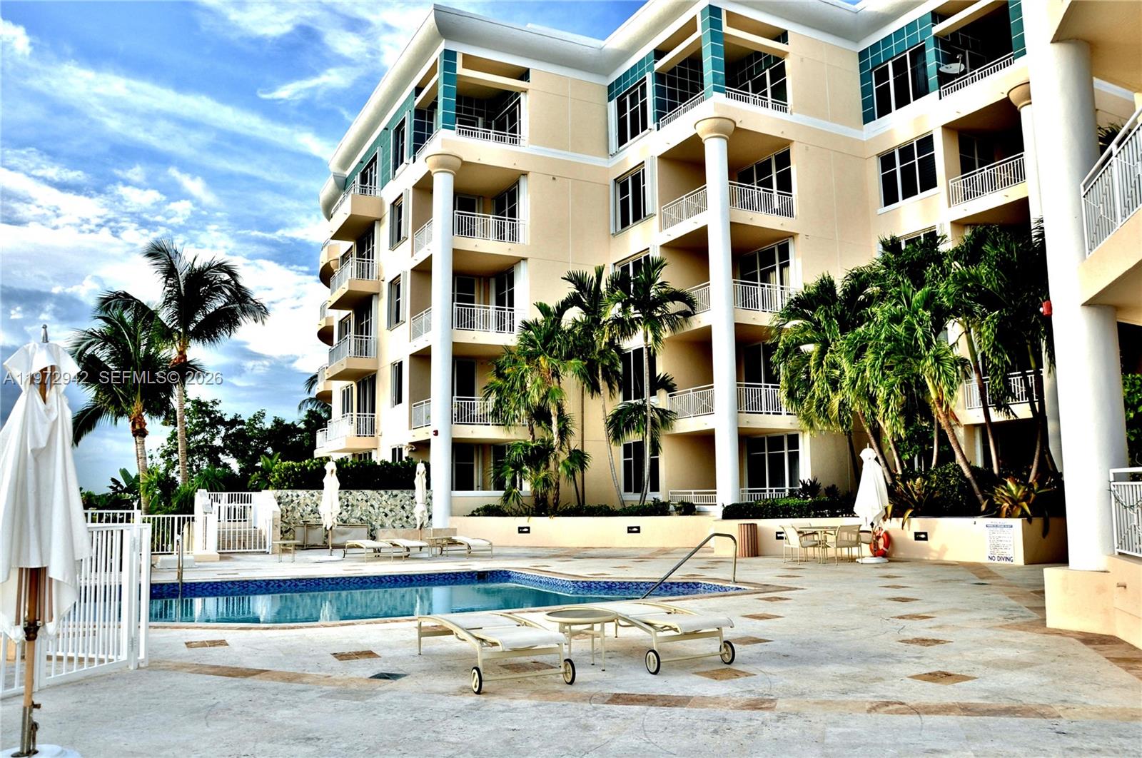 A multi-story apartment building features balconies overlooking a swimming pool with lounge chairs — 1 Century Ln # 310, Miami Beach FL 33139, MIAMI BEACH, FL