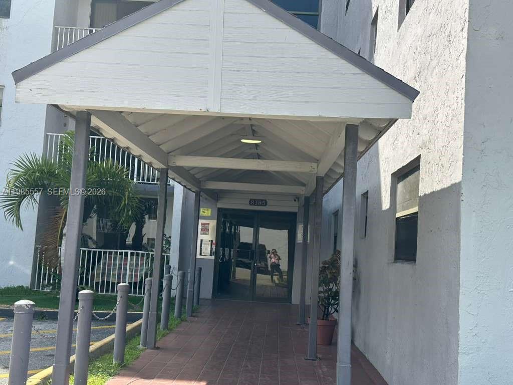 A covered walkway leads to the glass entrance doors of a multi-story residential building — 8185 NW 7th St # 319, Miami FL 33126, MIAMI, FL