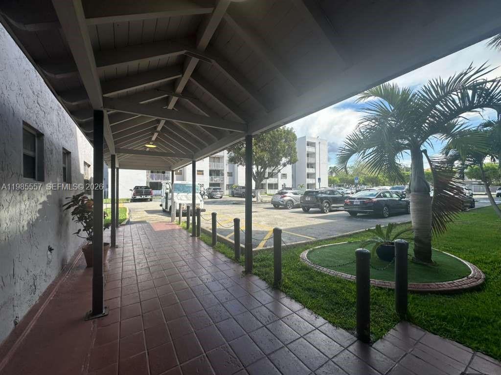 A covered walkway leads to a parking lot with several cars parked near apartment buildings — 8185 NW 7th St # 319, Miami FL 33126, MIAMI, FL