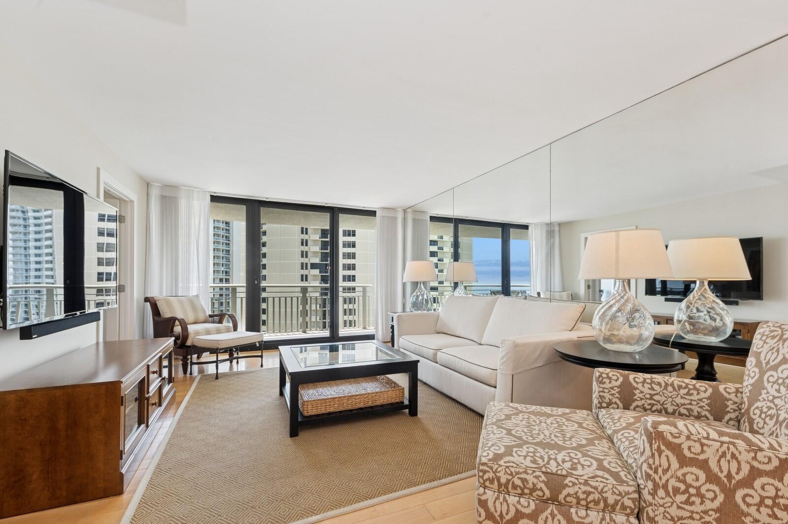 A living room features a white sofa, patterned armchairs, a glass-topped coffee table, and mirrored walls — 3000 N Ocean Drive # G, Singer Island FL 33404, SINGER ISLAND, FL