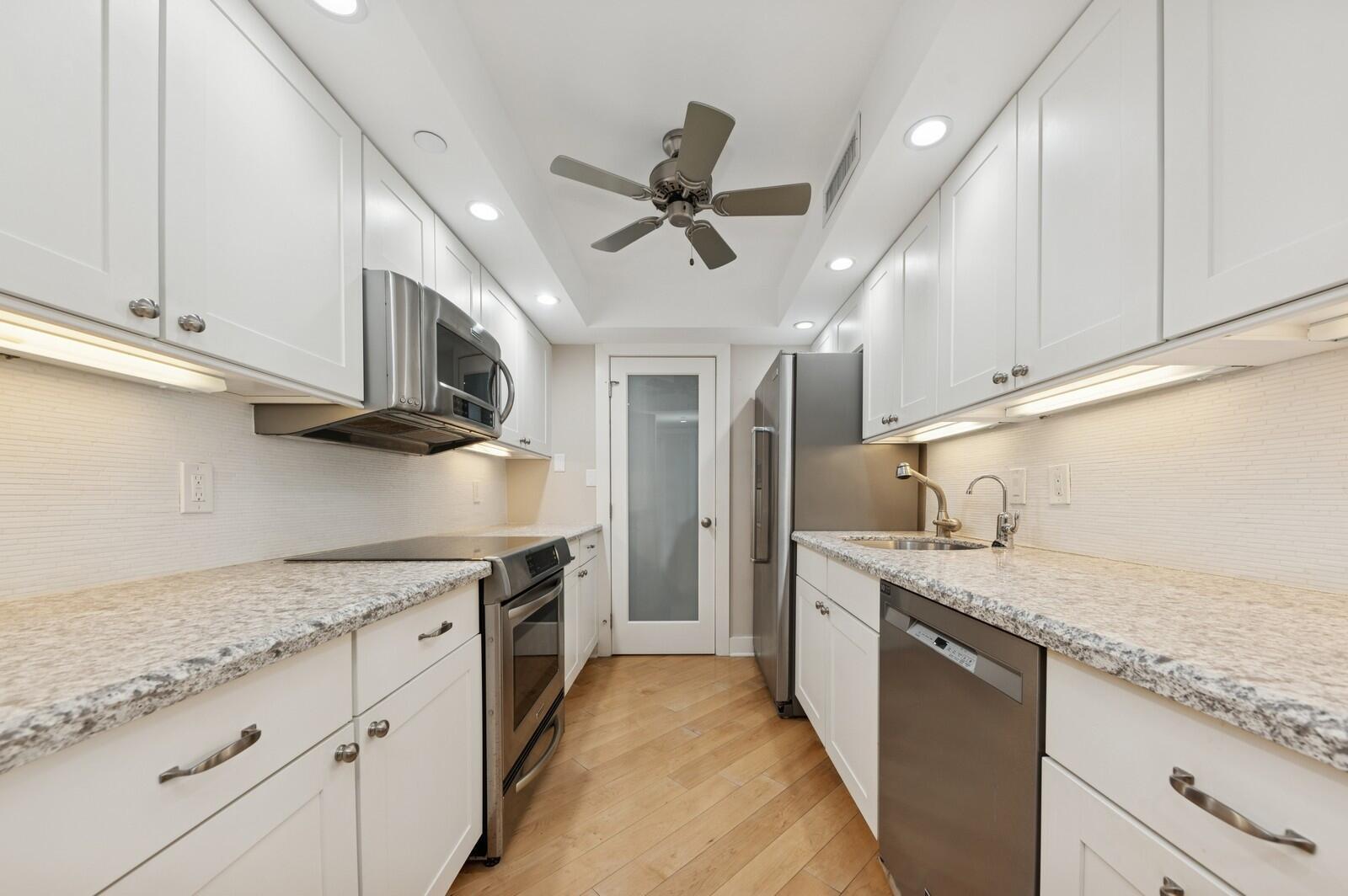 A galley kitchen features white cabinets, granite countertops, stainless steel appliances, and wood flooring — 3000 N Ocean Drive # G, Singer Island FL 33404, SINGER ISLAND, FL