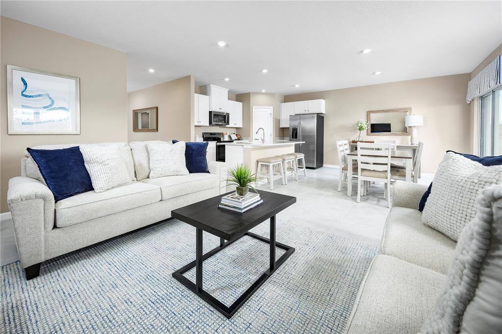 An open-concept living room and kitchen featuring light-colored sofas, a dark coffee table, and tile flooring — 512 171ST STREET E, BRADENTON, FL