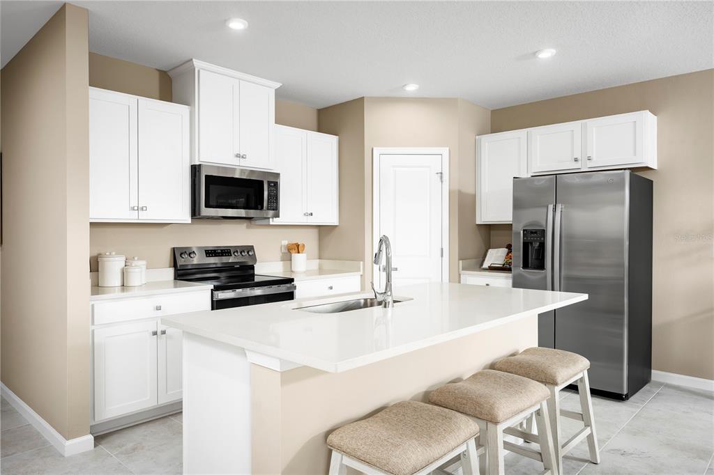 A modern kitchen features white cabinets, stainless steel appliances, a quartz island, and beige walls — 512 171ST STREET E, BRADENTON, FL