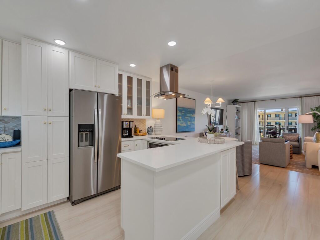 A modern kitchen with white cabinetry and stainless steel appliances opens into a living area — 4049 Ocean Drive # 402, Vero Beach FL 32963, VERO BEACH, FL