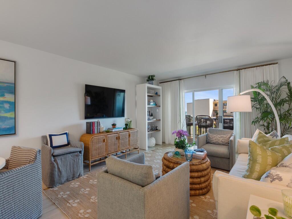 A living room features a television, wicker console, armchairs, a sofa, and a balcony view — 4049 Ocean Drive # 402, Vero Beach FL 32963, VERO BEACH, FL
