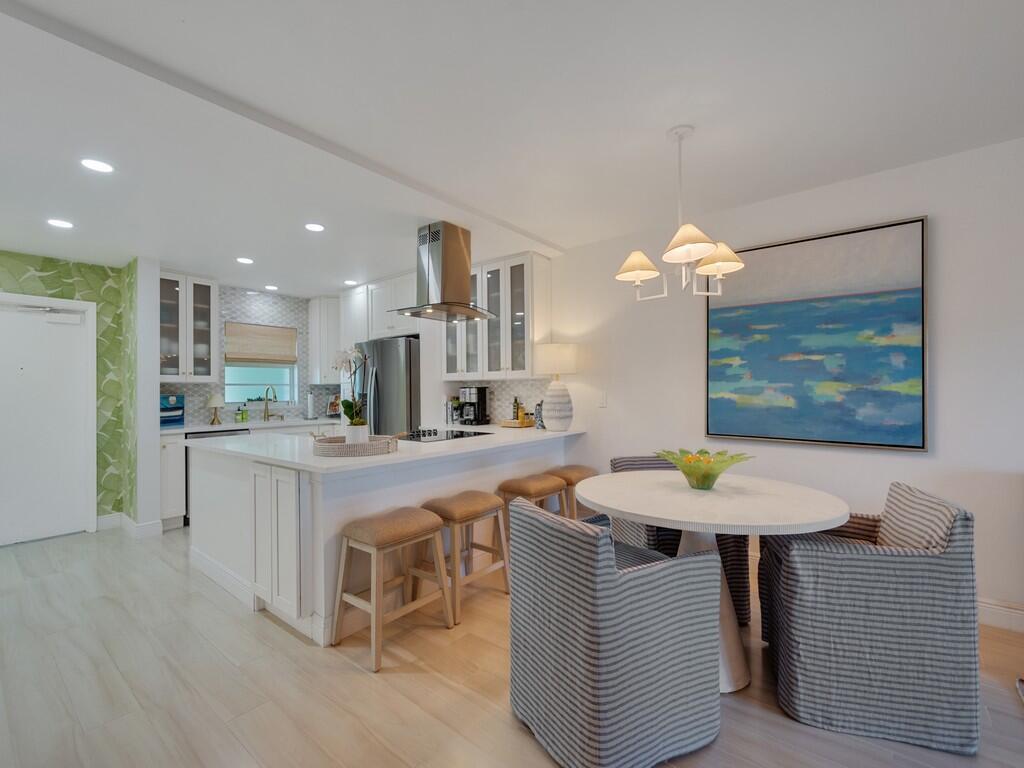 A modern kitchen features white cabinetry, a breakfast bar with stools, and an adjacent dining area — 4049 Ocean Drive # 402, Vero Beach FL 32963, VERO BEACH, FL