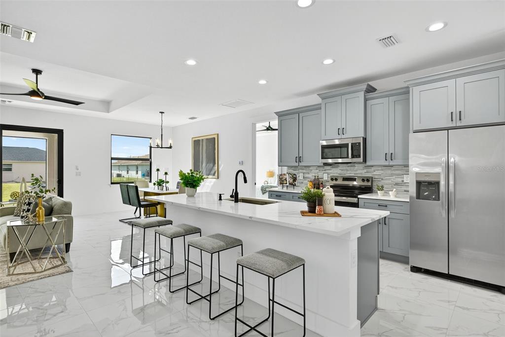 A modern kitchen features gray cabinets, a white marble island with barstools, and tile flooring — 4200 14TH STREET SW, LEHIGH ACRES, FL