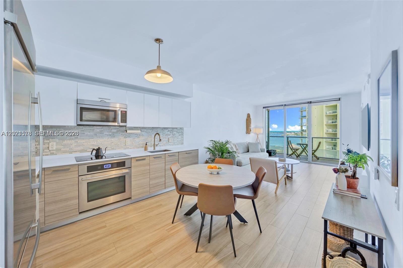 A modern open-concept kitchen and living area features light wood cabinetry and a balcony view — 1300 Brickell Bay Dr # 2104, Miami FL 33131, MIAMI, FL