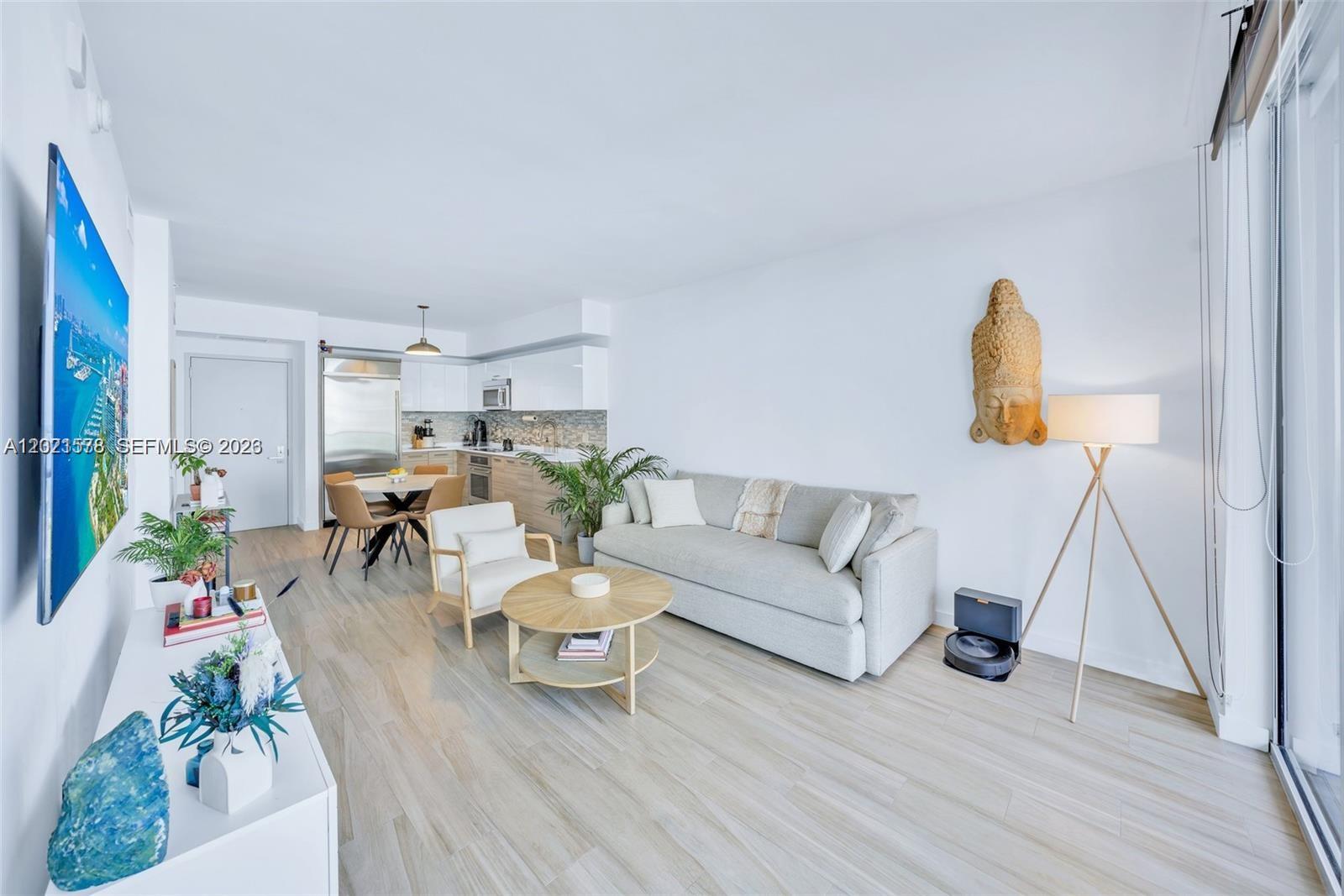 A bright living room features light wood flooring, a neutral sofa, and an open kitchen — 1300 Brickell Bay Dr # 2104, Miami FL 33131, MIAMI, FL
