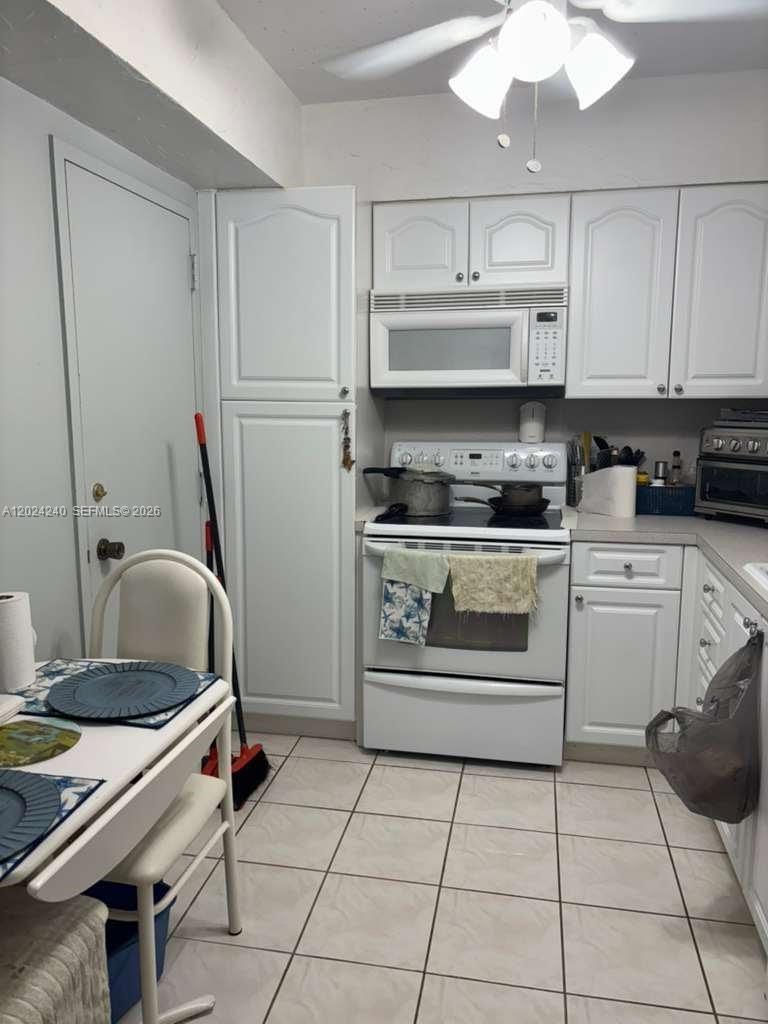 A kitchen with white cabinets, a white stove, a microwave, and a small dining table — 1985 S Ocean Dr # 3B, Hallandale Beach FL 33009, HALLANDALE BEACH, FL