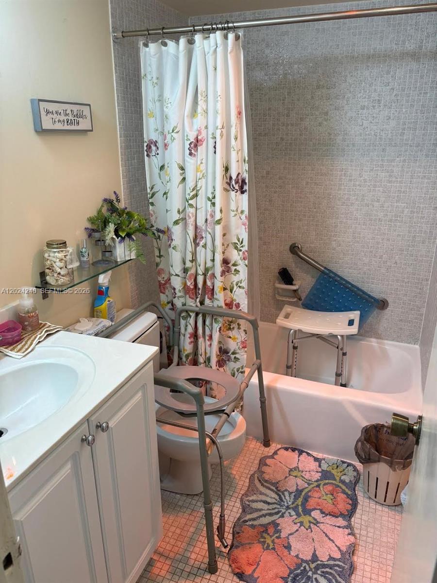 A bathroom features a floral shower curtain, a tiled tub surround, and medical safety equipment — 1985 S Ocean Dr # 3B, Hallandale Beach FL 33009, HALLANDALE BEACH, FL