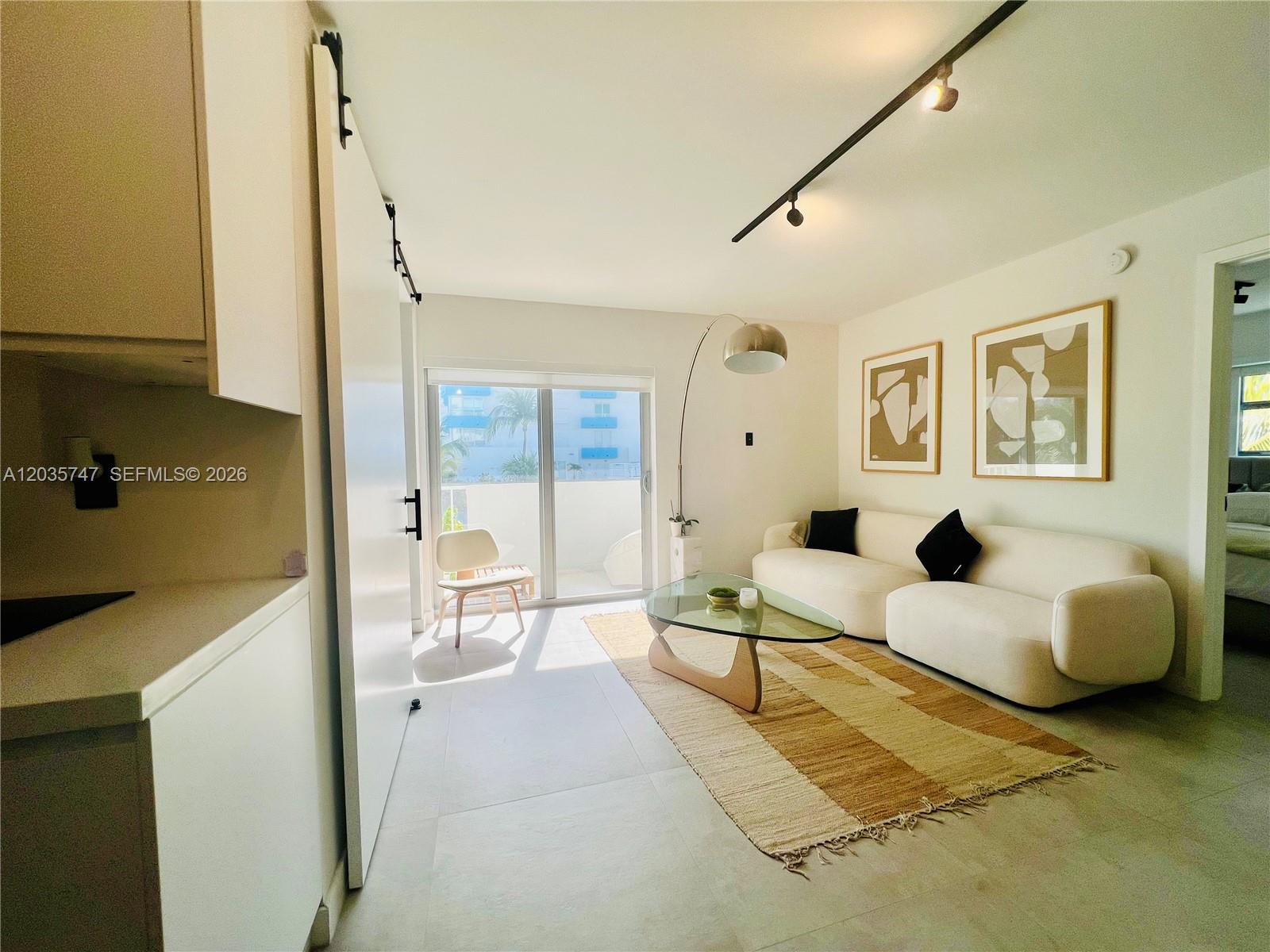 A living room features a white sofa, glass coffee table, and a sliding barn door — 240 Collins Ave # 4A, Miami Beach FL 33139, MIAMI BEACH, FL
