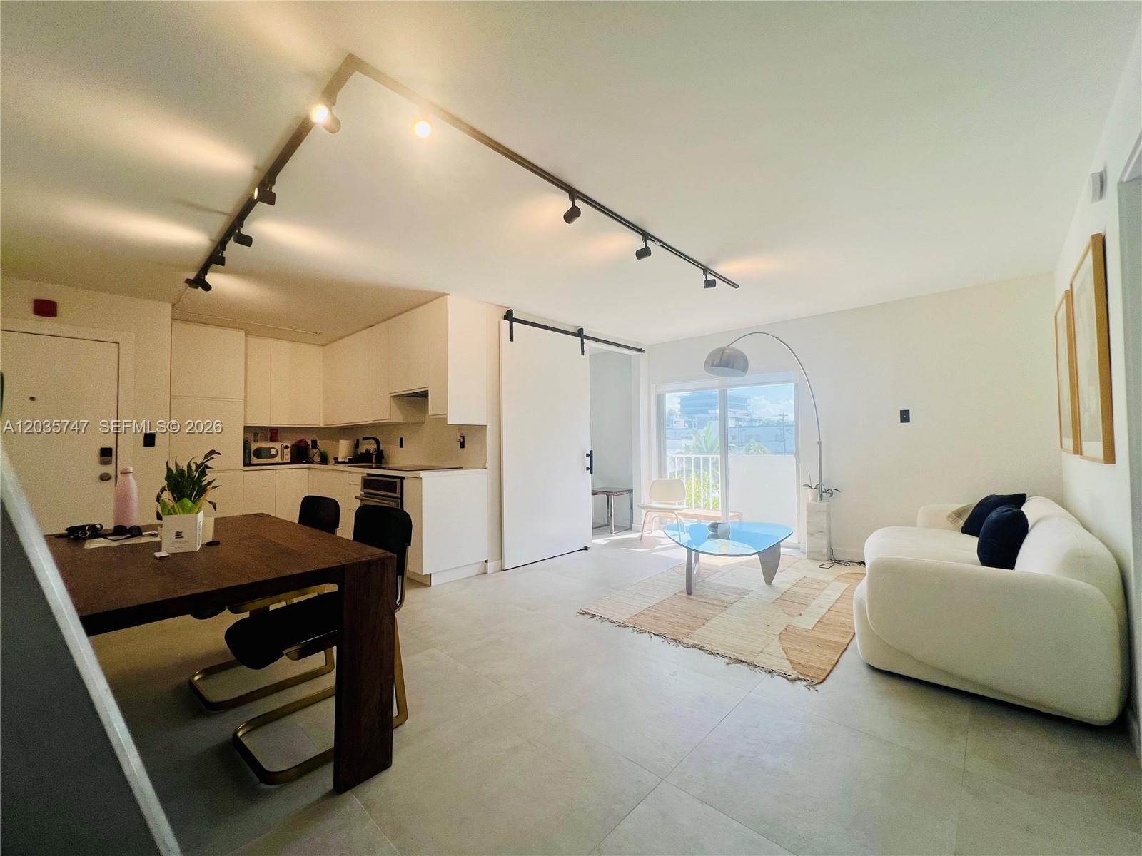 An open-concept living and dining area features white cabinetry, tile flooring, and a sliding door — 240 Collins Ave # 4A, Miami Beach FL 33139, MIAMI BEACH, FL