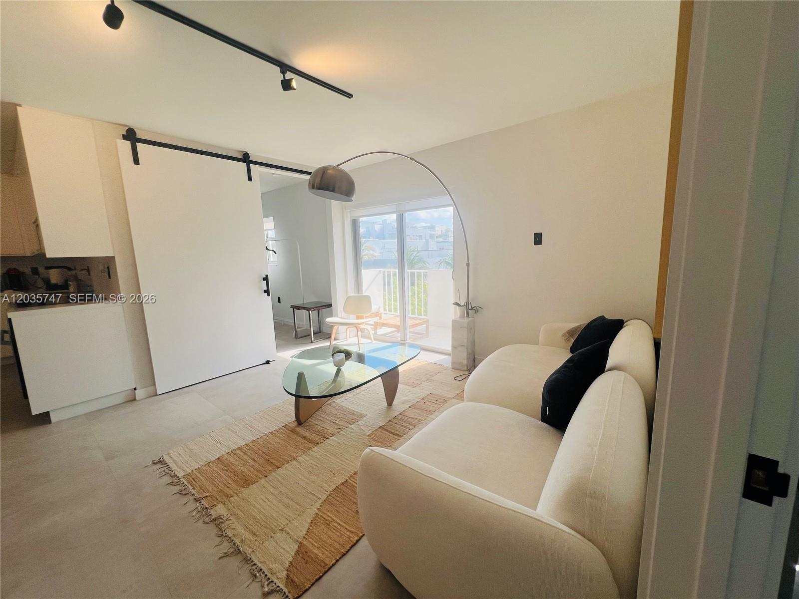 A modern living room features a white sofa, glass coffee table, and a sliding door — 240 Collins Ave # 4A, Miami Beach FL 33139, MIAMI BEACH, FL