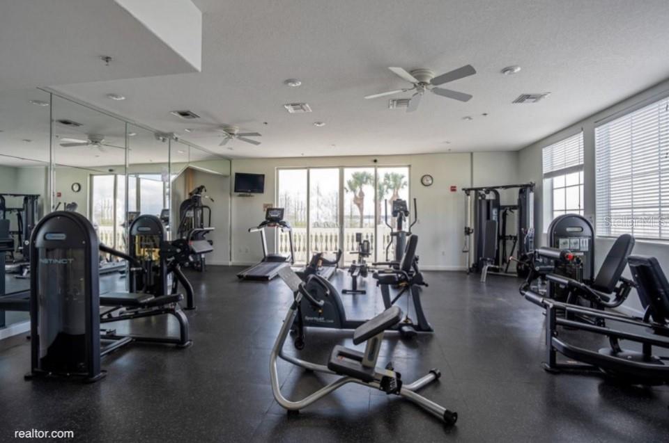 A fitness center with various exercise machines, mirrored walls, ceiling fans, and large windows — 8760 THE ESPLANADE UNIT 51, ORLANDO, FL