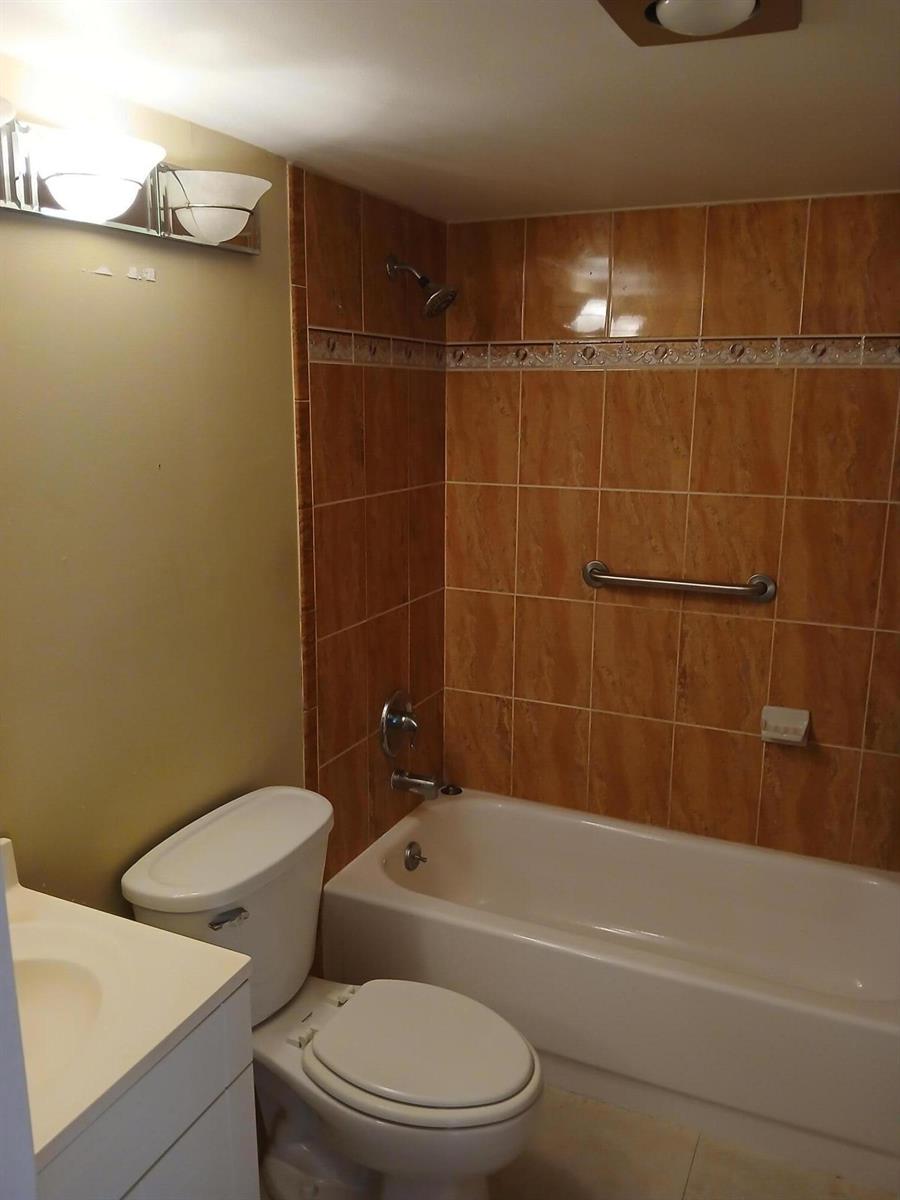 A bathroom features a white toilet, a vanity, and a bathtub with brown tiled walls — 250 Durham # F, Deerfield Beach FL 33442, DEERFIELD BEACH, FL