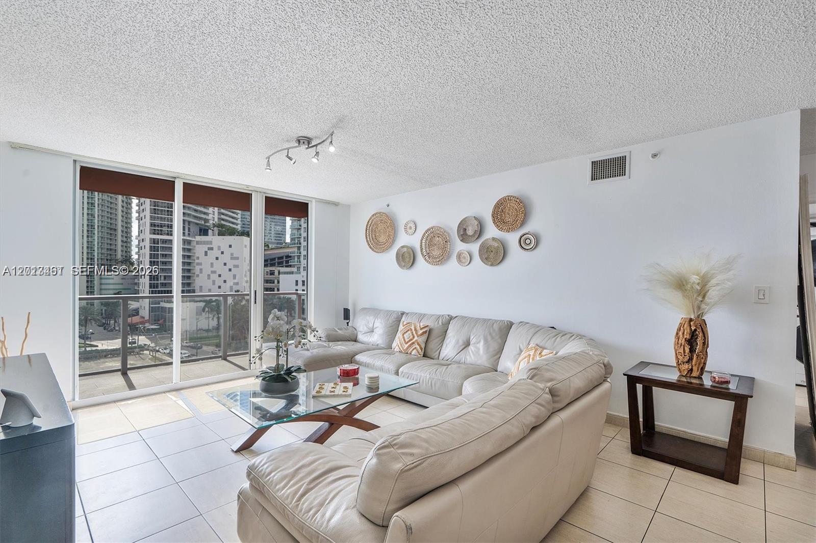 A living room features a large sectional sofa, a glass coffee table, and wall-mounted decor — 1155 Brickell Bay Dr # 603, Miami FL 33131, MIAMI, FL
