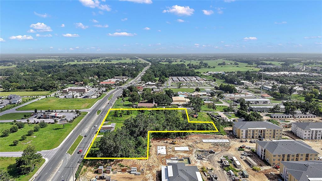 An aerial view shows a vacant, tree-covered lot outlined in yellow next to a construction site — 11535 N US 301, OXFORD, FL