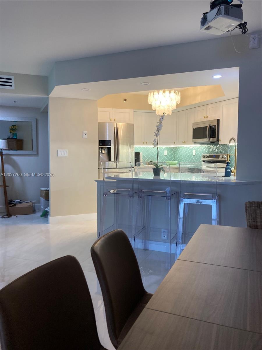 A kitchen with white cabinets, a teal backsplash, and a breakfast bar with clear stools — 6767 Collins Ave # 1701, Miami Beach FL 33141, MIAMI BEACH, FL