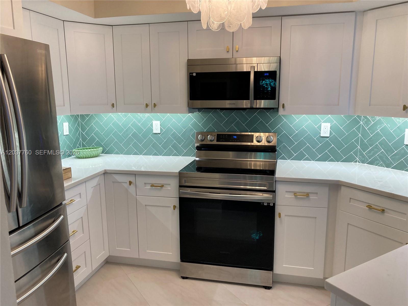 A kitchen features white cabinets, stainless steel appliances, and a green herringbone tile backsplash — 6767 Collins Ave # 1701, Miami Beach FL 33141, MIAMI BEACH, FL