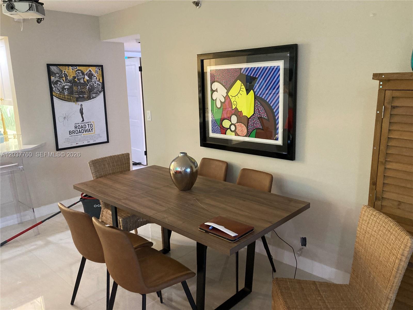 A dining room features a wooden table with mixed chairs, wall art, and a projector — 6767 Collins Ave # 1701, Miami Beach FL 33141, MIAMI BEACH, FL