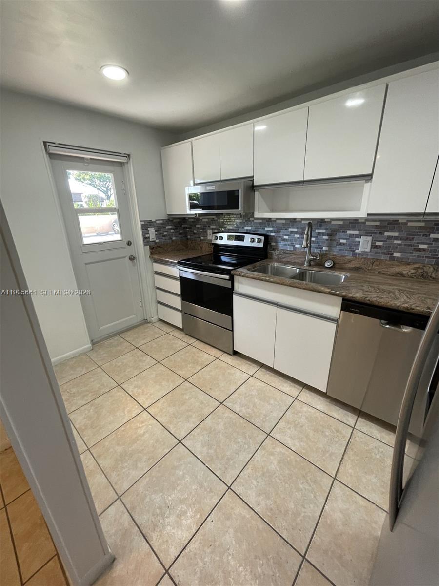 A kitchen features white cabinets, stainless steel appliances, a tiled backsplash, and beige floor tiles — 4500 N Federal Hwy # 102A, Lighthouse Point FL 33064, LIGHTHOUSE POINT, FL