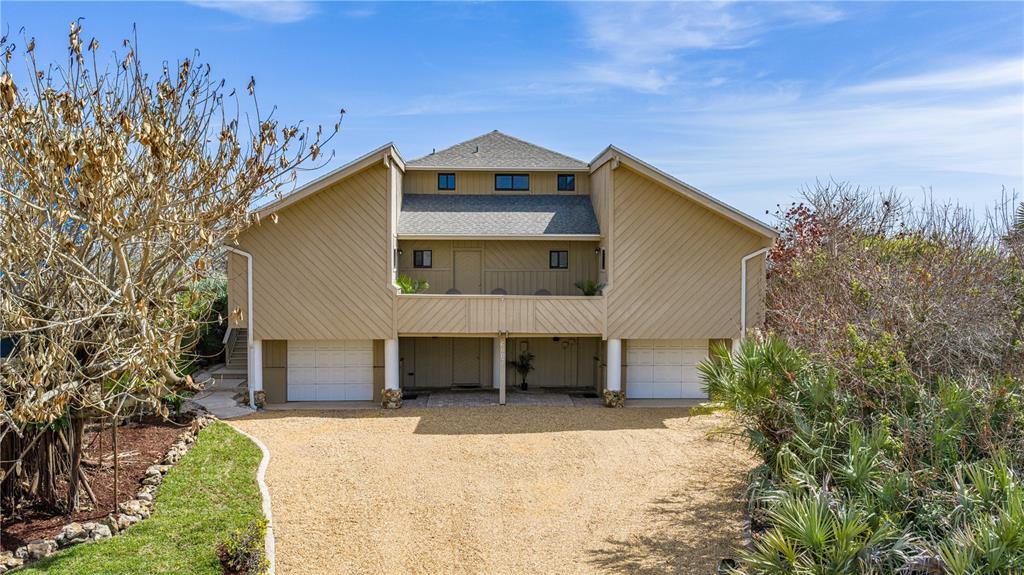 A two-story house with a gravel driveway, elevated living area, and two ground-level garage doors — 6007 S ATLANTIC AVENUE, NEW SMYRNA BEACH, FL