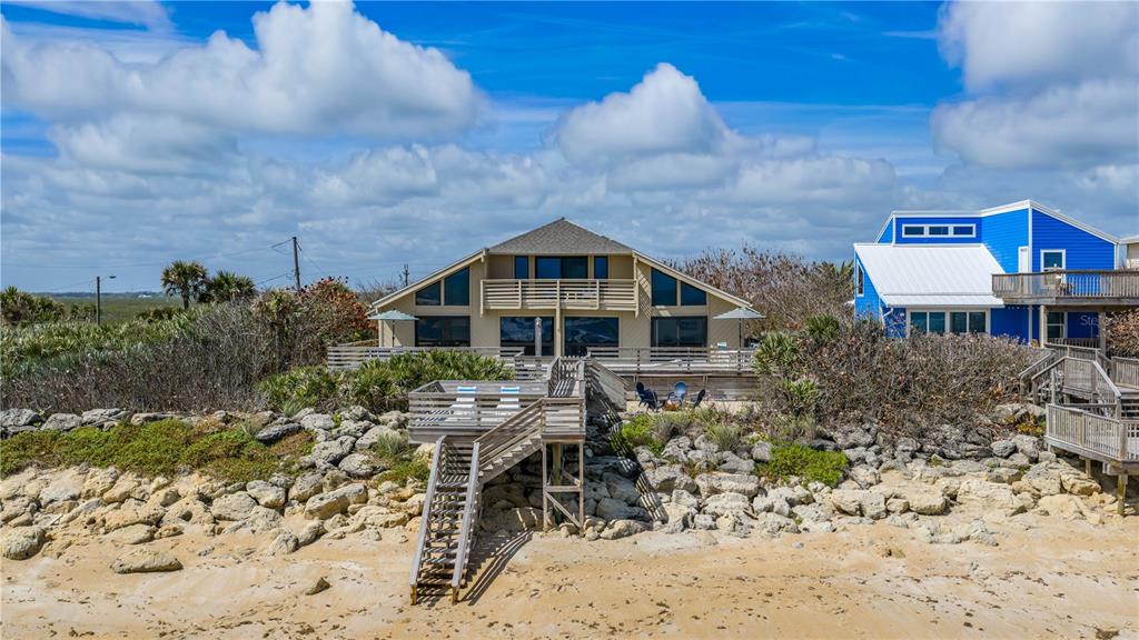A tan beach house with a wooden staircase leading down to the sandy shore — 6007 S ATLANTIC AVENUE, NEW SMYRNA BEACH, FL