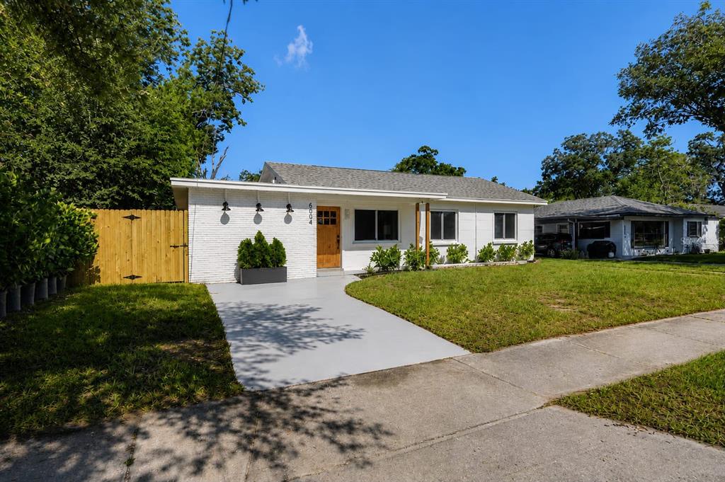 A white brick, single-story house features a wooden front door and a gray concrete driveway — 6504 N 20TH STREET, TAMPA, FL