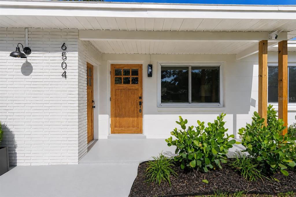 A white brick house exterior features a wooden front door and a covered porch — 6504 N 20TH STREET, TAMPA, FL