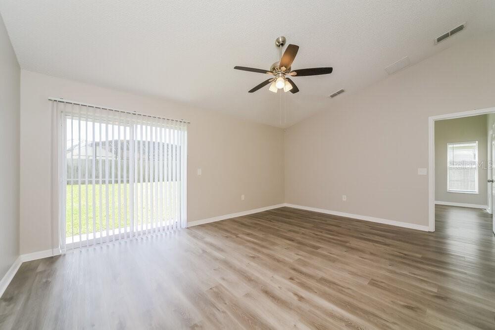 An empty living room features light-colored walls, wood-look flooring, a ceiling fan, and sliding doors — 5537 WILLOW BEND TRAIL, KISSIMMEE, FL