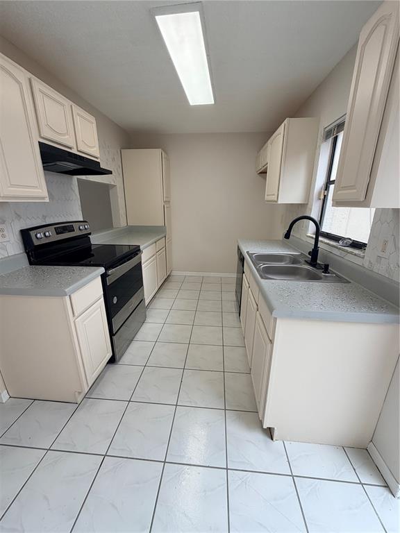 A galley kitchen features off-white cabinets, gray countertops, a black stove, and white tiled floors — 1625 LONG RIDGE COURT UNIT 271, ORLANDO, FL