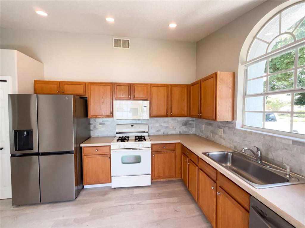 A kitchen features wood cabinets, stainless steel appliances, a white stove, and a large window — 3028 SAMOSA HILL CIRCLE, CLERMONT, FL